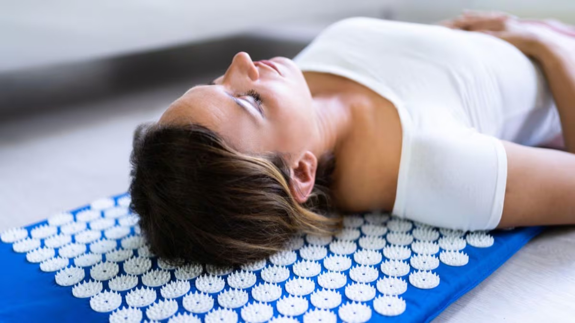 mujer tumbada sobre alfombra de acupresión en casa relajando la espalda